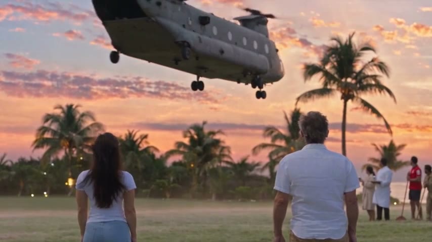 Seen from behind, Nora and an older man in a white shirt watch a twin-rotor helicopter lift off a palm-lined lawn at sunset.